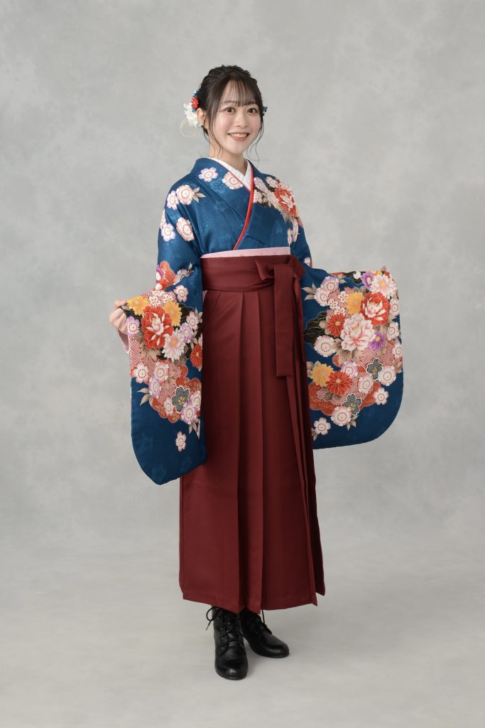 キモノモード町田店の卒業袴を着たお客様のスタジオ写真。両袖を広げて着物の柄を見せている。青い着物と、えんじ色の袴の組み合わせ。