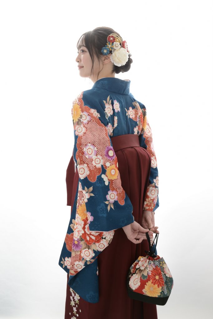 キモノモード町田店の卒業袴を着た後ろ姿のスタジオ写真。青い袴用の着物にえんじ色の袴。桜の刺繍袴。