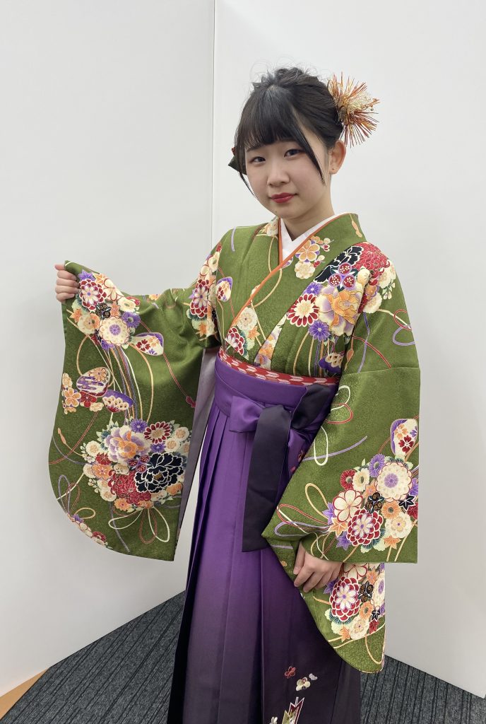 キモノモード町田店の専門学校卒業袴のお客様写真。緑色の小振袖に紫色の袴を合わせ、右袖を広げている写真。
