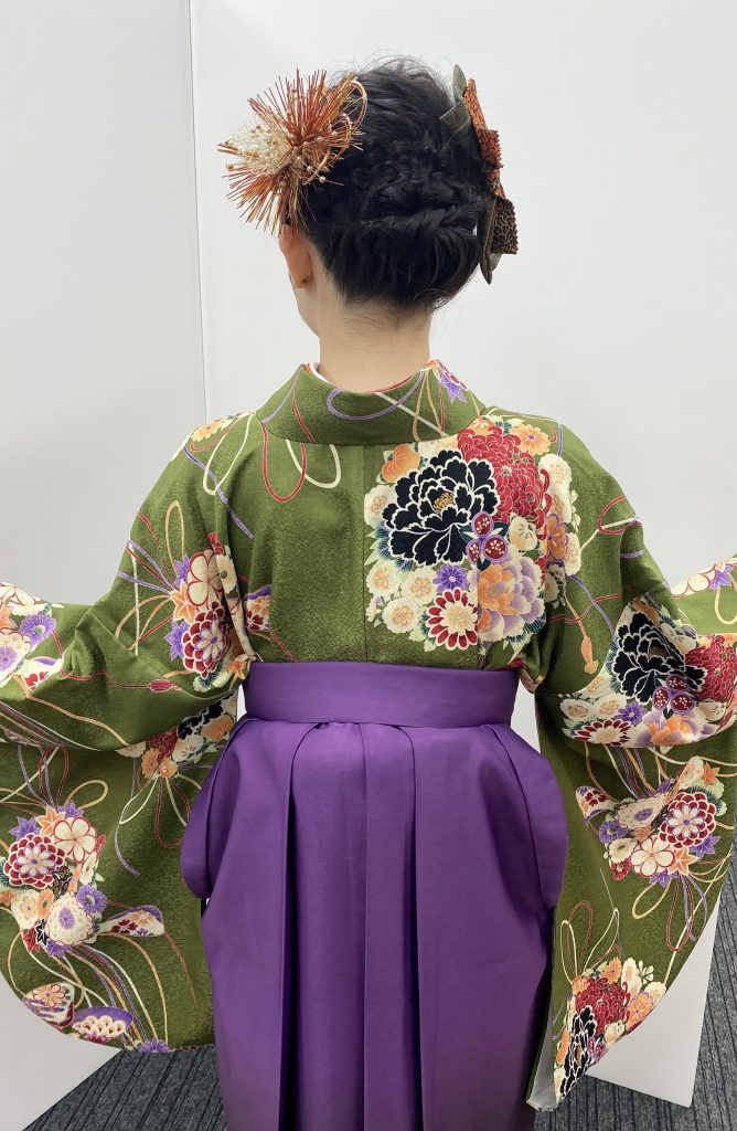 キモノモード町田店の専門学校卒業袴のお客様コーディネート写真。抹茶色の振袖を着て両袖を広げた後姿の写真。紫色の袴の写真。